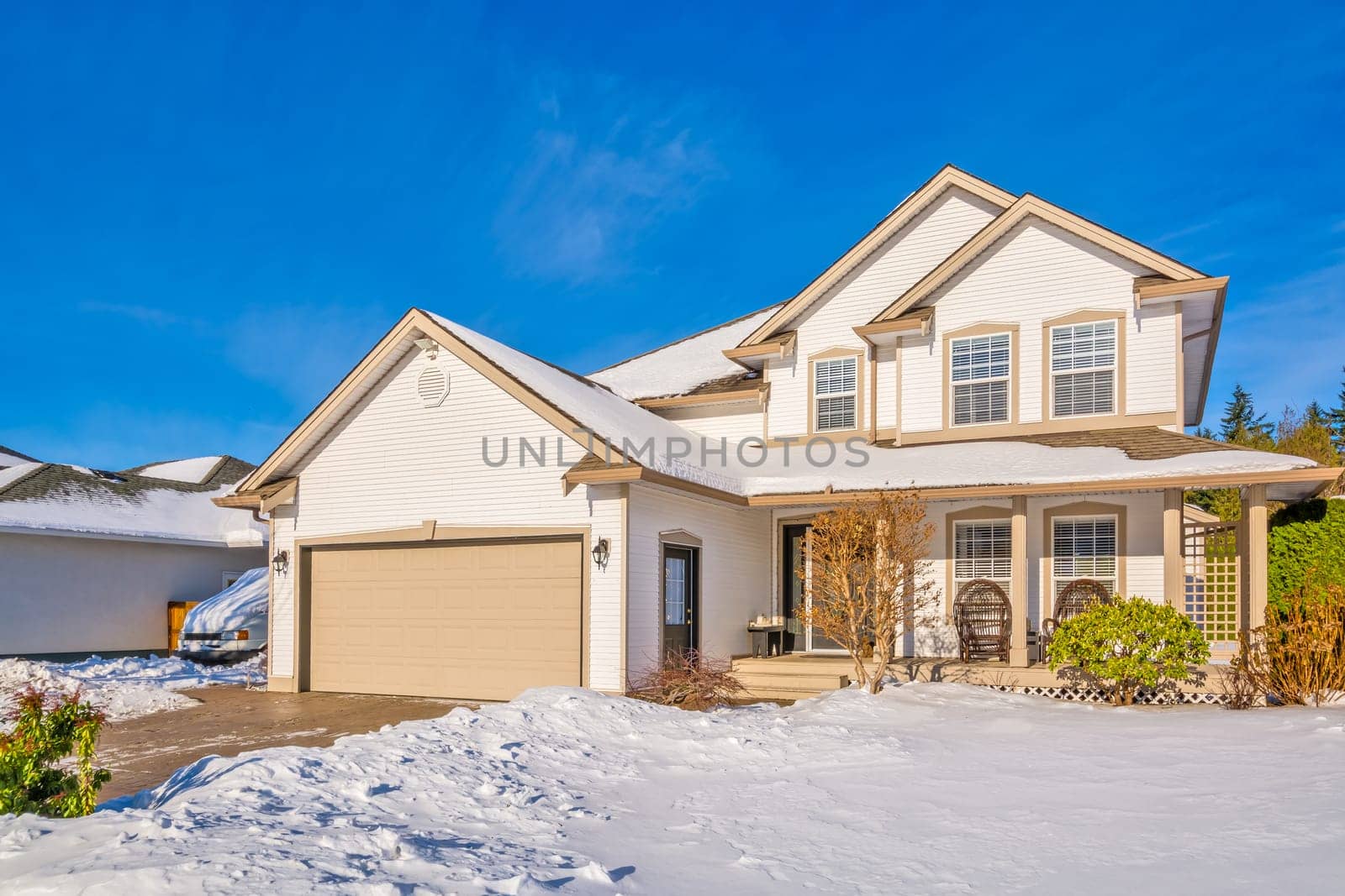 Family house with driveway and front yard in snow on winter sunny day. Luxury residential house with double garage on winter season