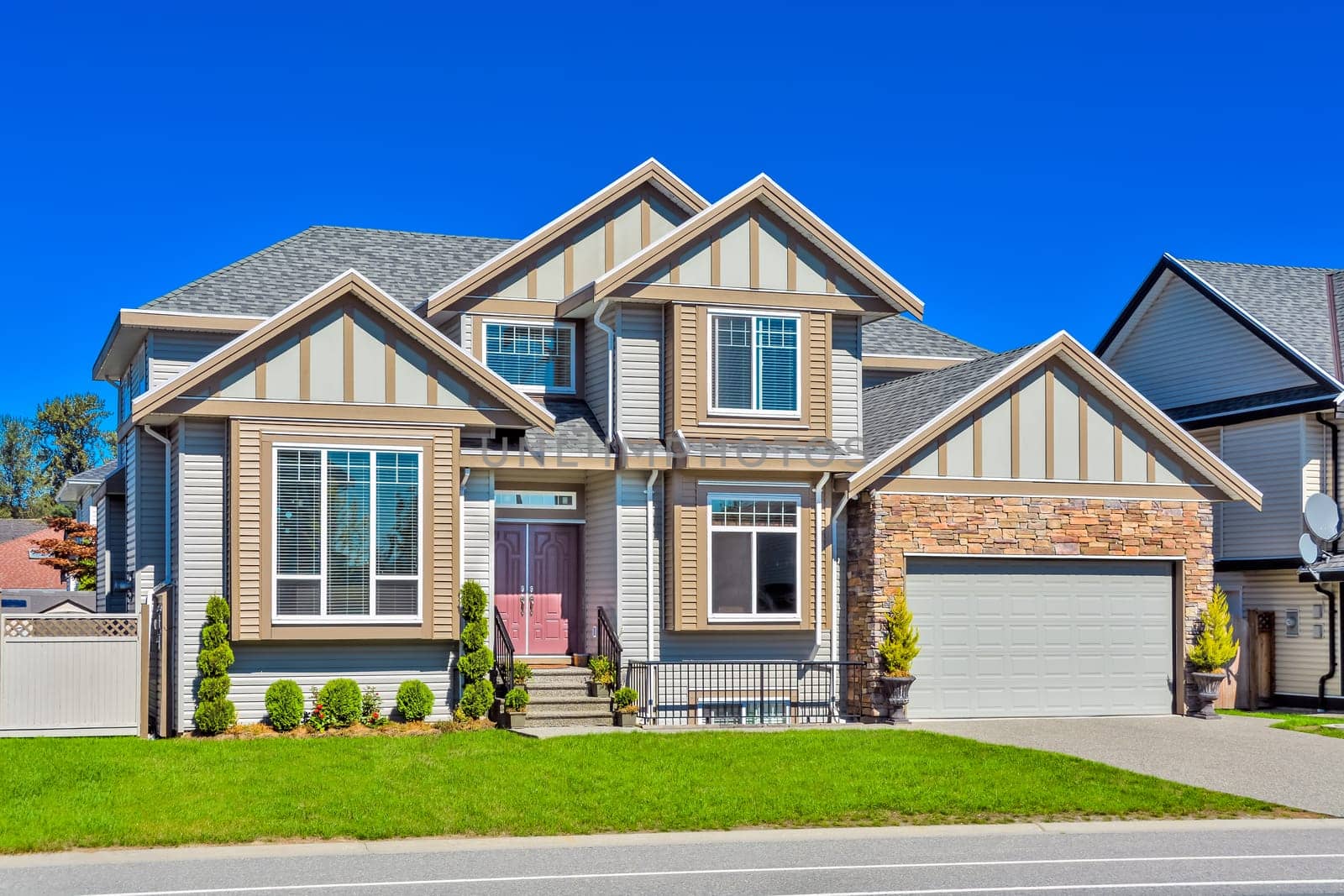 A perfect neighborhood. Suburban family house with concrete driveway and green lawn in front on blue sky background.