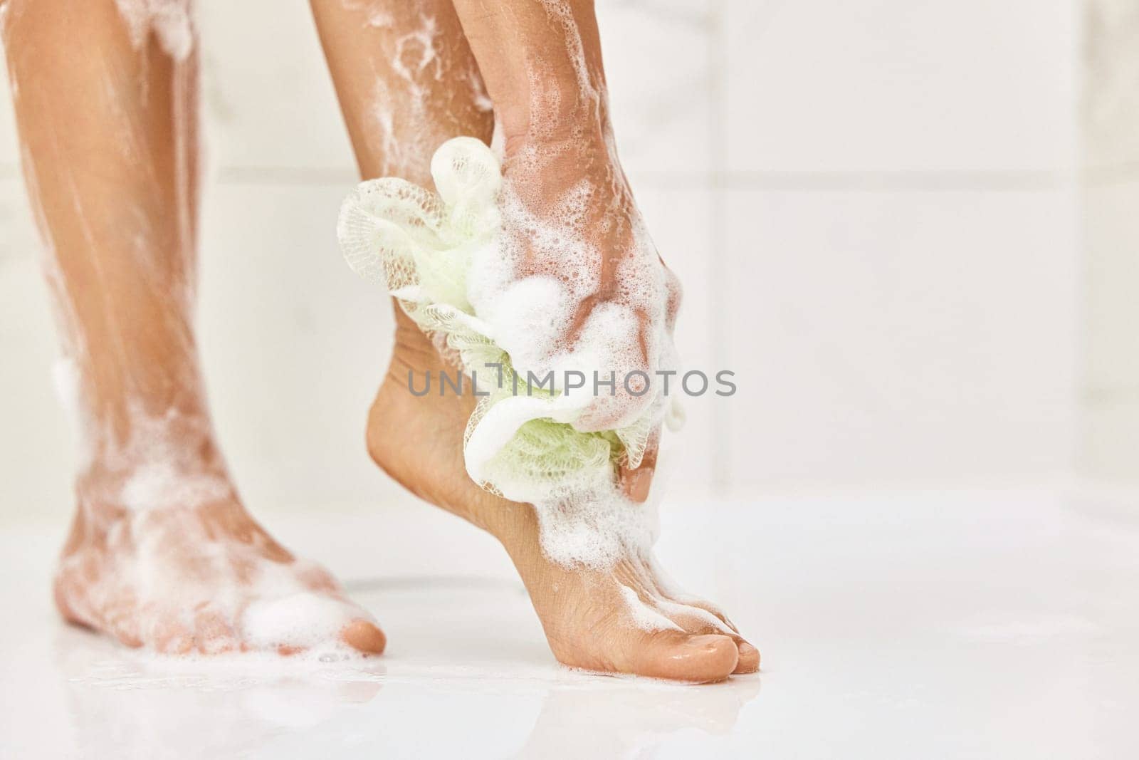 Woman washing her legs with foam bubbles and bath sponge while taking shower in the bathroom