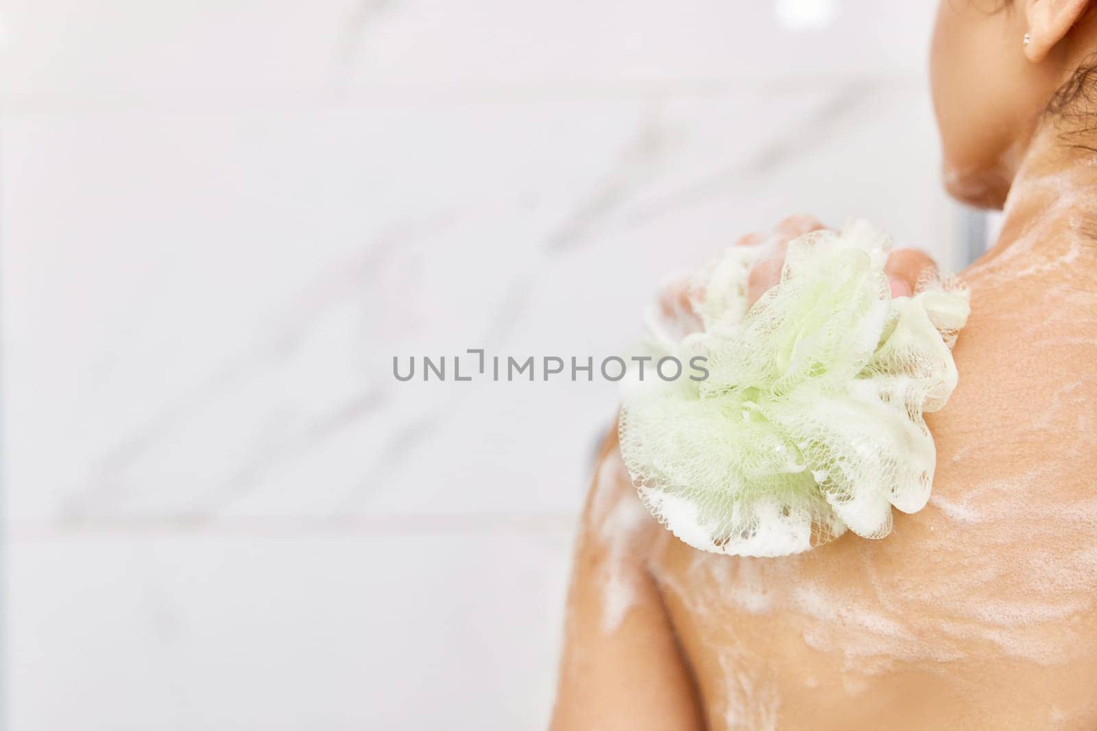 Caucasian woman washing her shoulder with sponge in white shower, copy space. Spa procedure