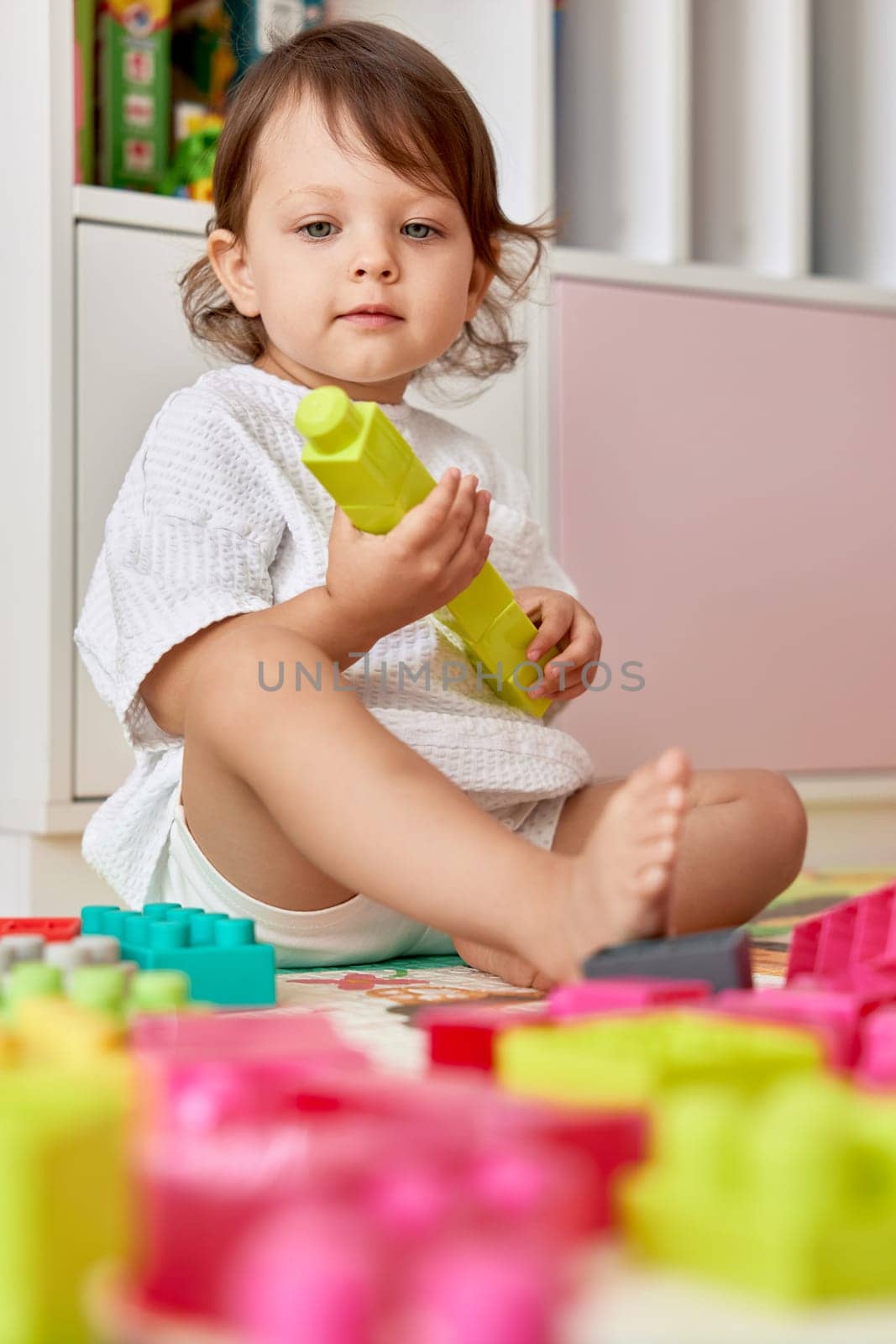 cute baby girl playing with colorful toys bricks at home. kid building green tower