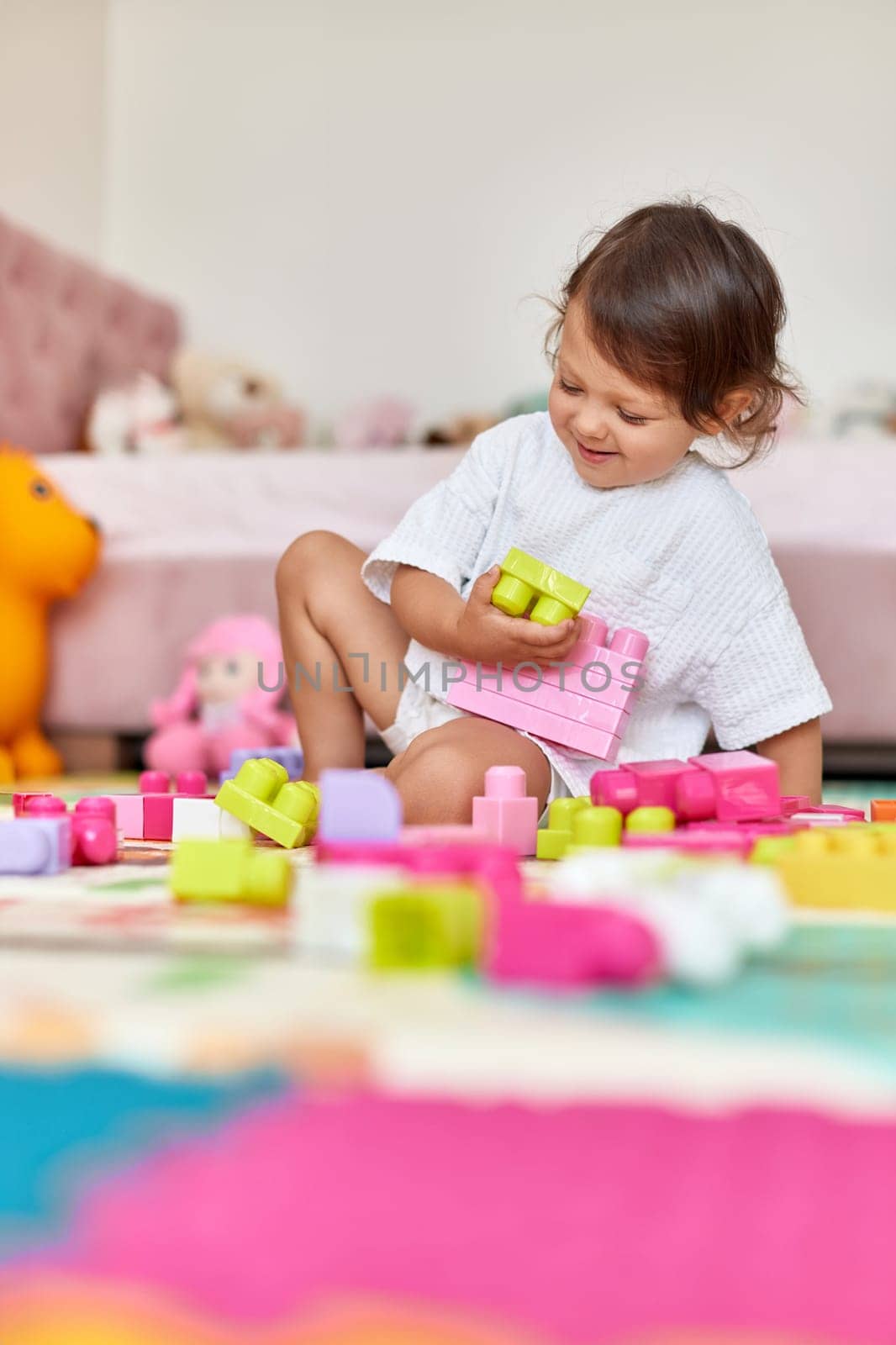 cute baby girl playing with colorful toy blocks in her room