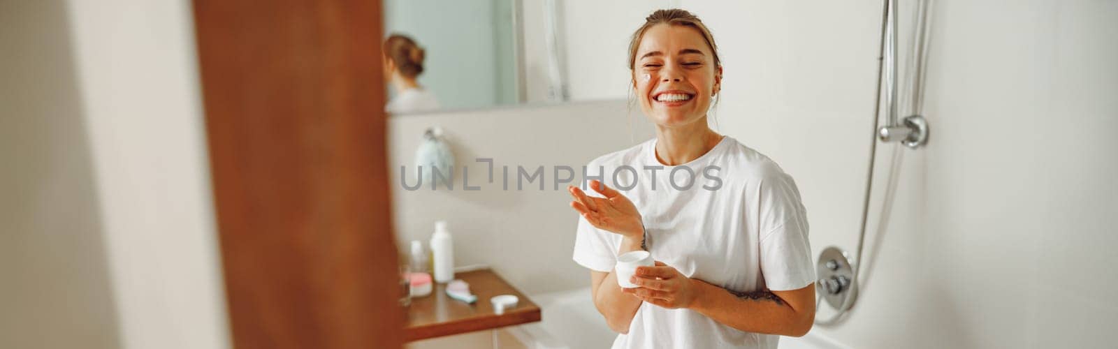 Smiling woman holding jar with skincare cream in hands. Home beauty routine
