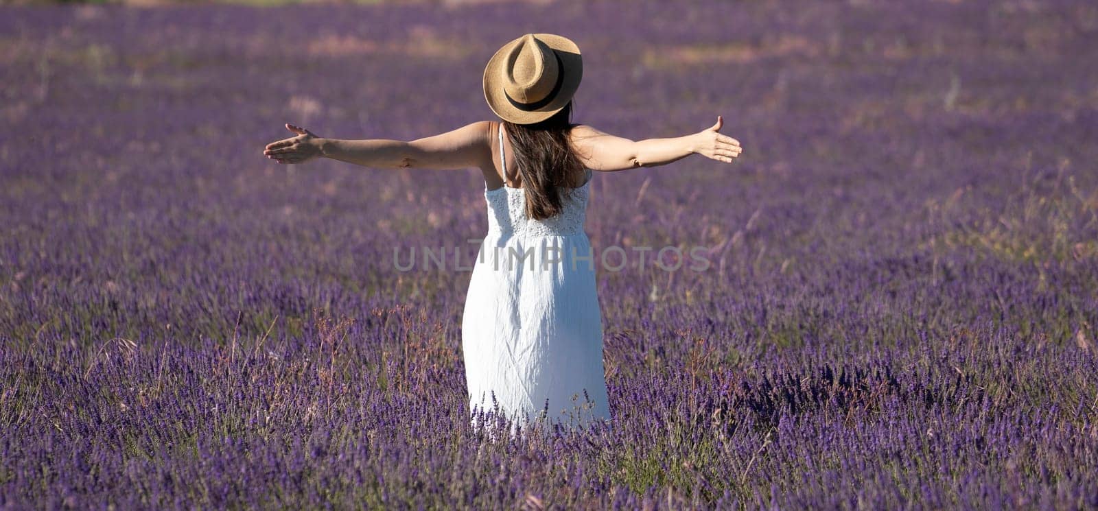 Rear view of a happy woman in white dress standing on a lavender field with open arms. Freedom and happiness concepts.