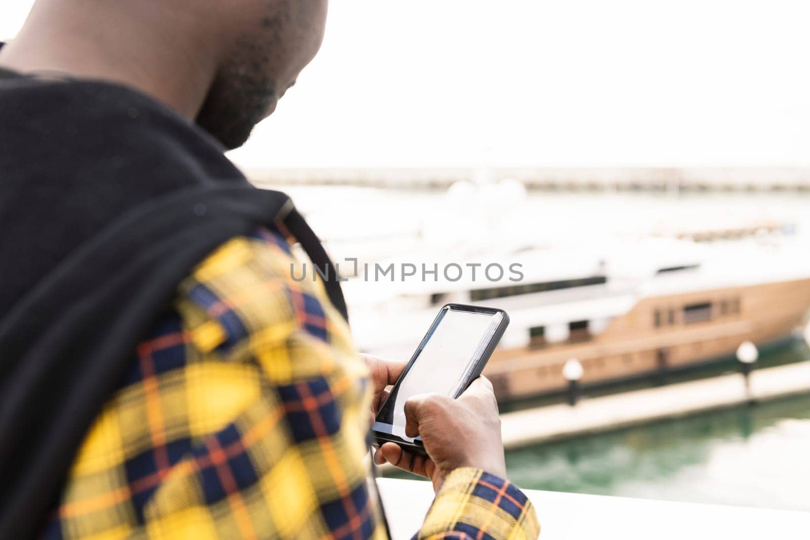 unrecognizable black man consulting his smartphone in front of the yachts in the marina, lifestyle concept and technology