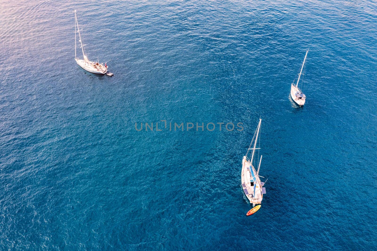 Aerial view of anchored sailing yacht in emerald sea. Aerial view of a boat. Outdoor water sports, yachting. Aerial view of anchoring yacht in open water. Ocean and sea travel and transportation