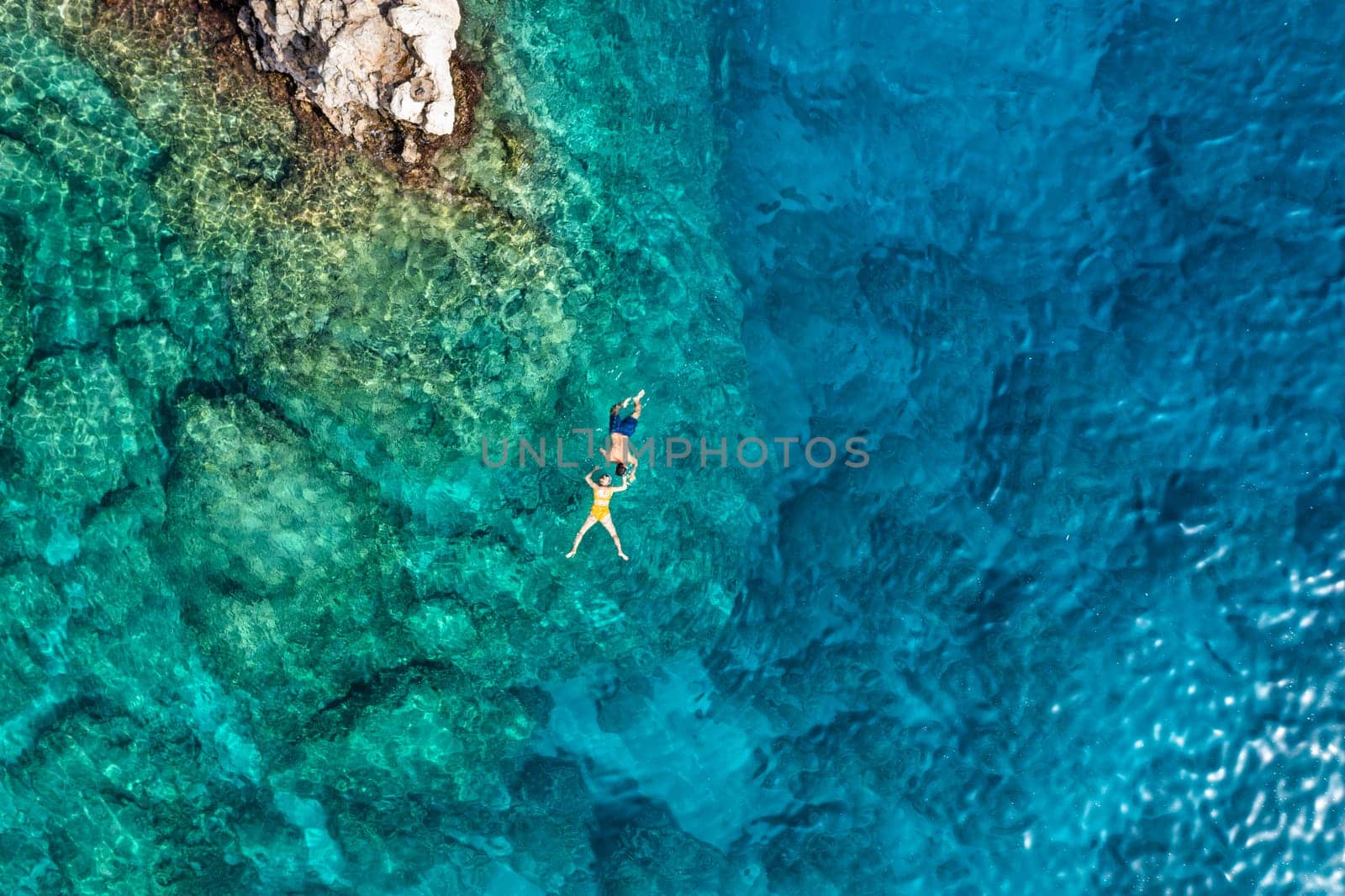 Aerial view of a young couple snorkeling above coral reef reaching deeper parts of the crystal clear water, Rhodes, Greece. Aerial drone view of a couple snorkeling swimming in crystal clear water.