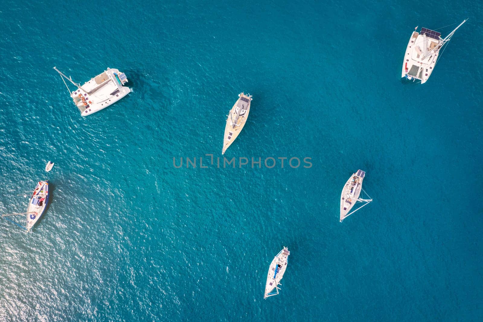 Yacht anchoring in crystal clear turquoise water in front of the tropical island, alternative lifestyle, living on a boat. Aerial view of yacht at anchor on turquoise water, showing luxury, wealth.