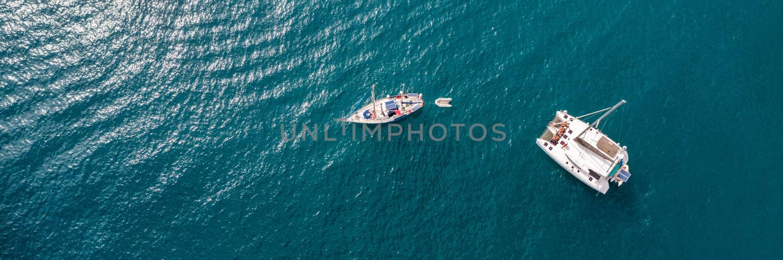 Yacht anchoring in crystal clear turquoise water in front of the tropical island, alternative lifestyle, living on a boat. Aerial view of yacht at anchor on turquoise water, showing luxury, wealth.