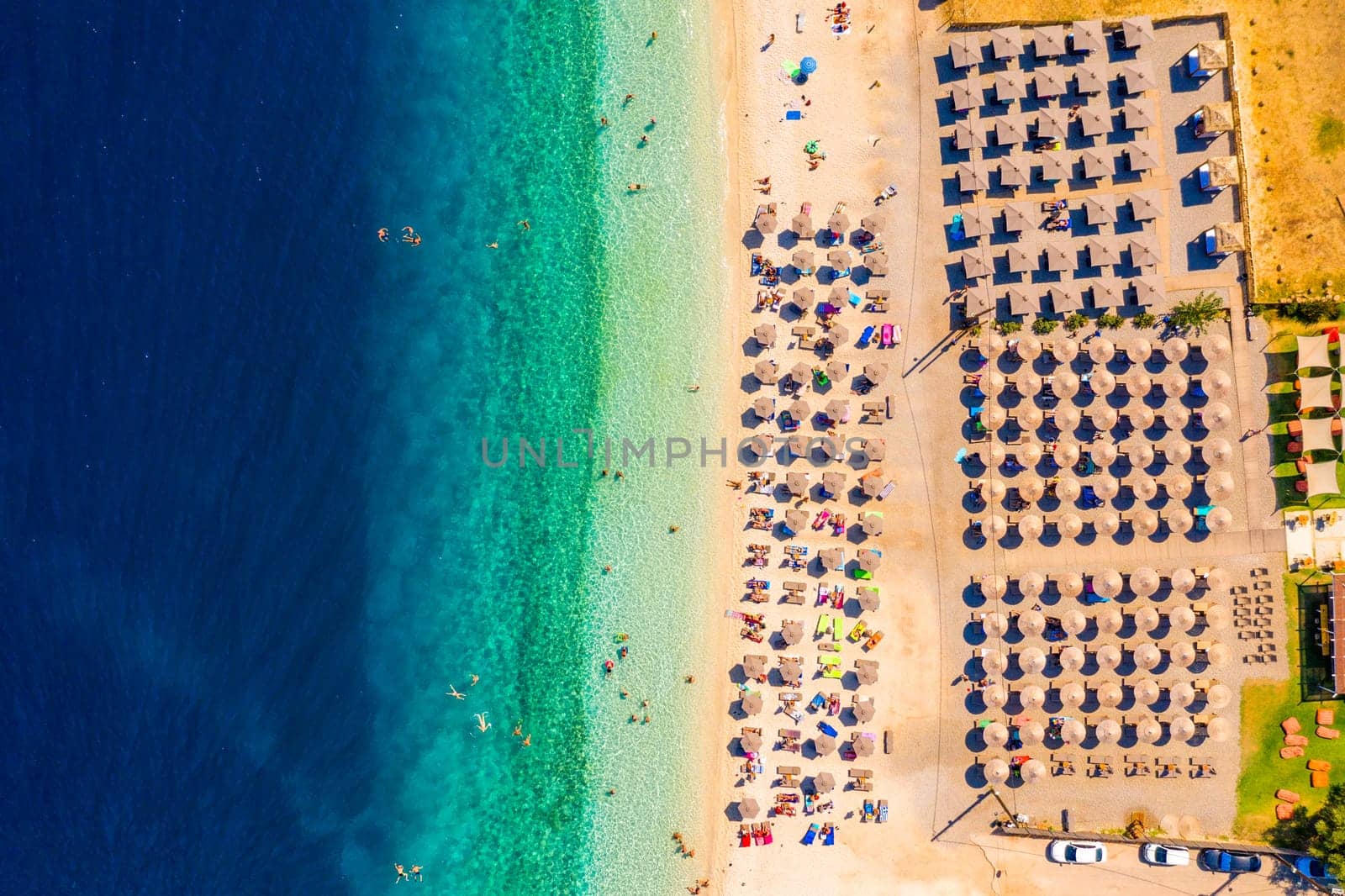 View from above, stunning aerial view of an amazing beach with beach umbrellas and turquoise clear water. Top view on sun loungers under umbrellas on the sandy beach. Concept of summer vacation. 