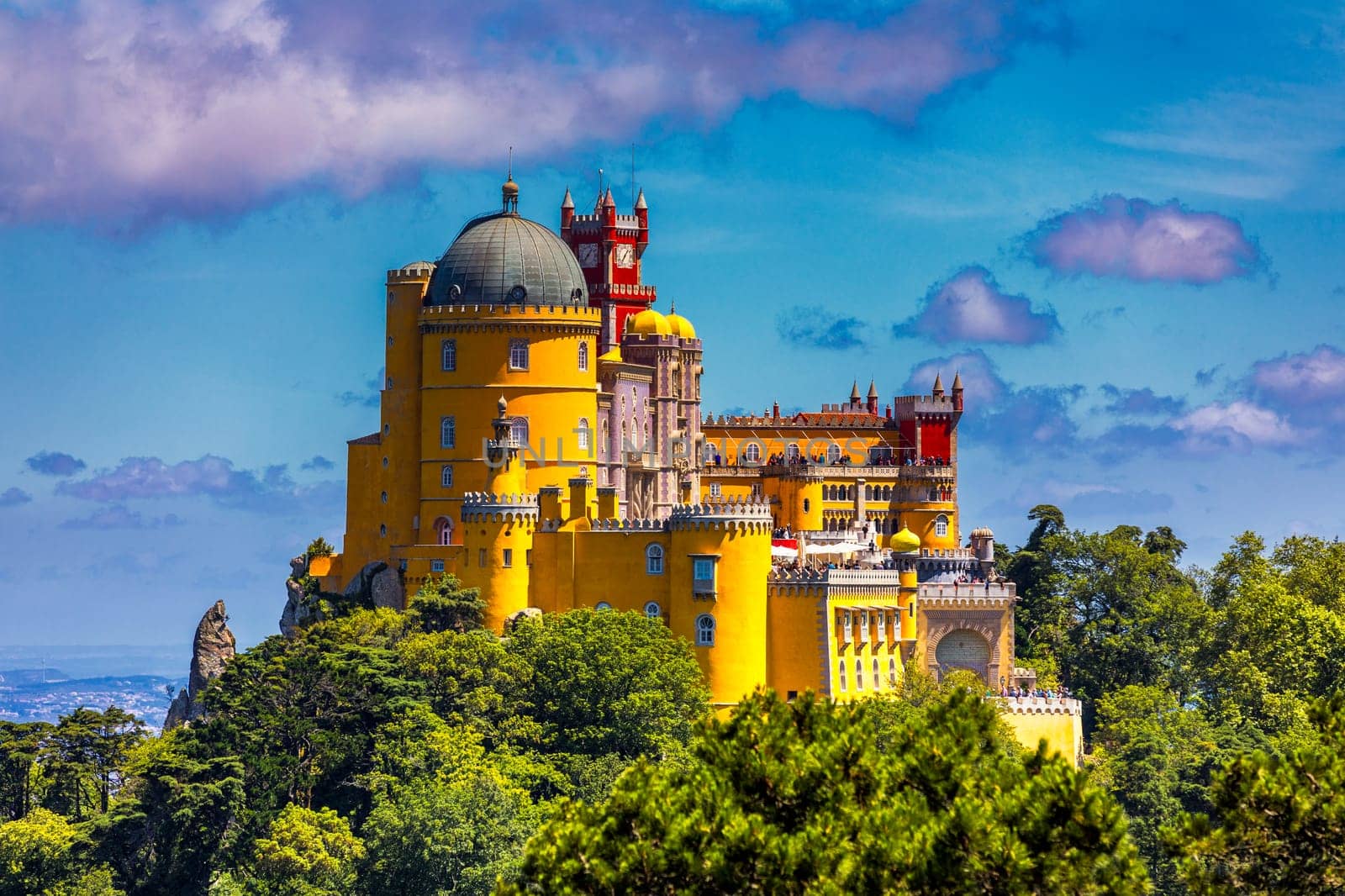 Famous historic Pena palace part of cultural site of Sintra against sunset sky in Portugal. Panoramic View Of Pena Palace, Sintra, Portugal. Pena National Palace at sunset, Sintra, Portugal. 