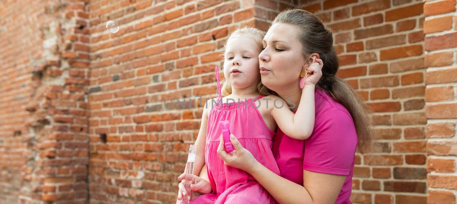 Blonde little girl with cochlear implant playing with her mother outdoor. Hear impairment deaf and health concept. Diversity and inclusion. Copy space.