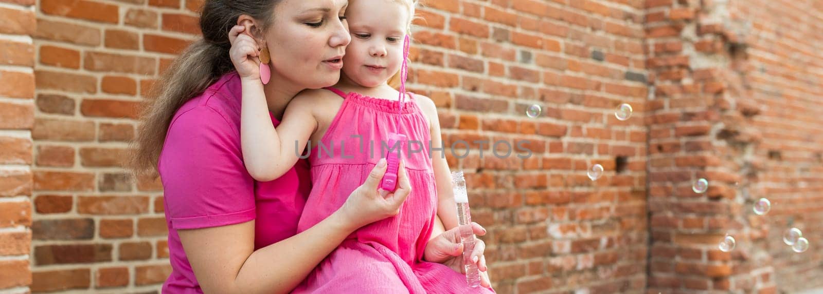 Blonde little girl with cochlear implant playing with her mother outdoor. Hear impairment deaf and health concept. Diversity and inclusion. Copy space.