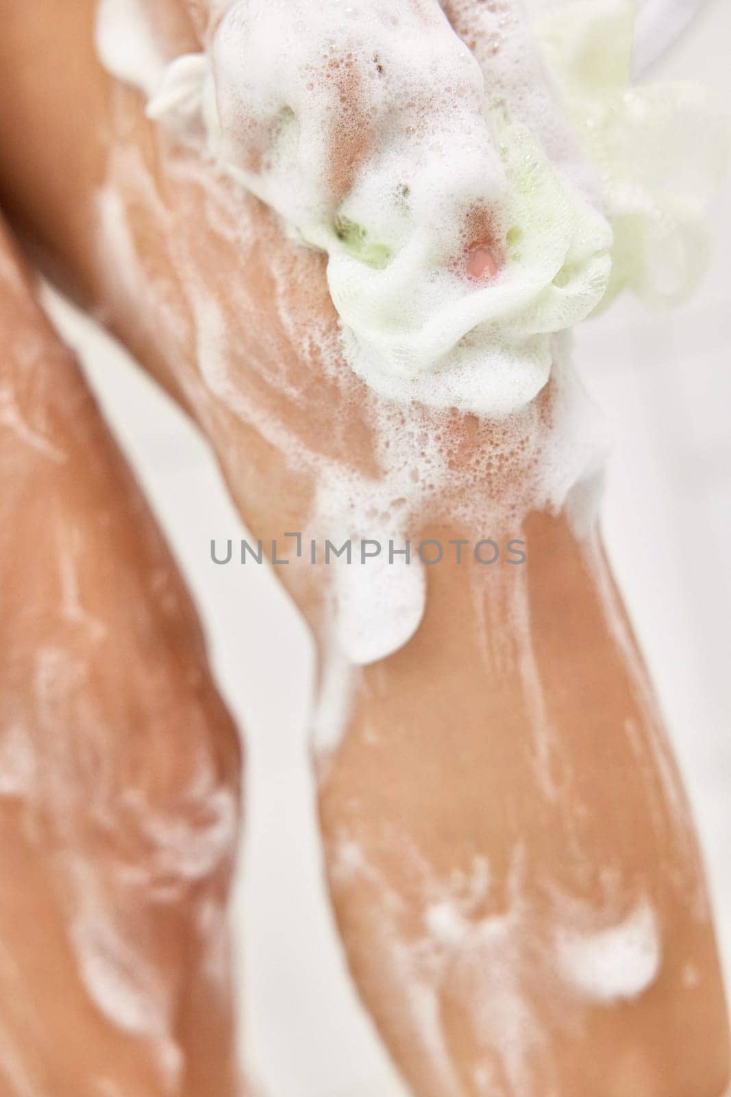 Woman washing her legs with foam bubbles and bath sponge while taking shower in the bathroom
