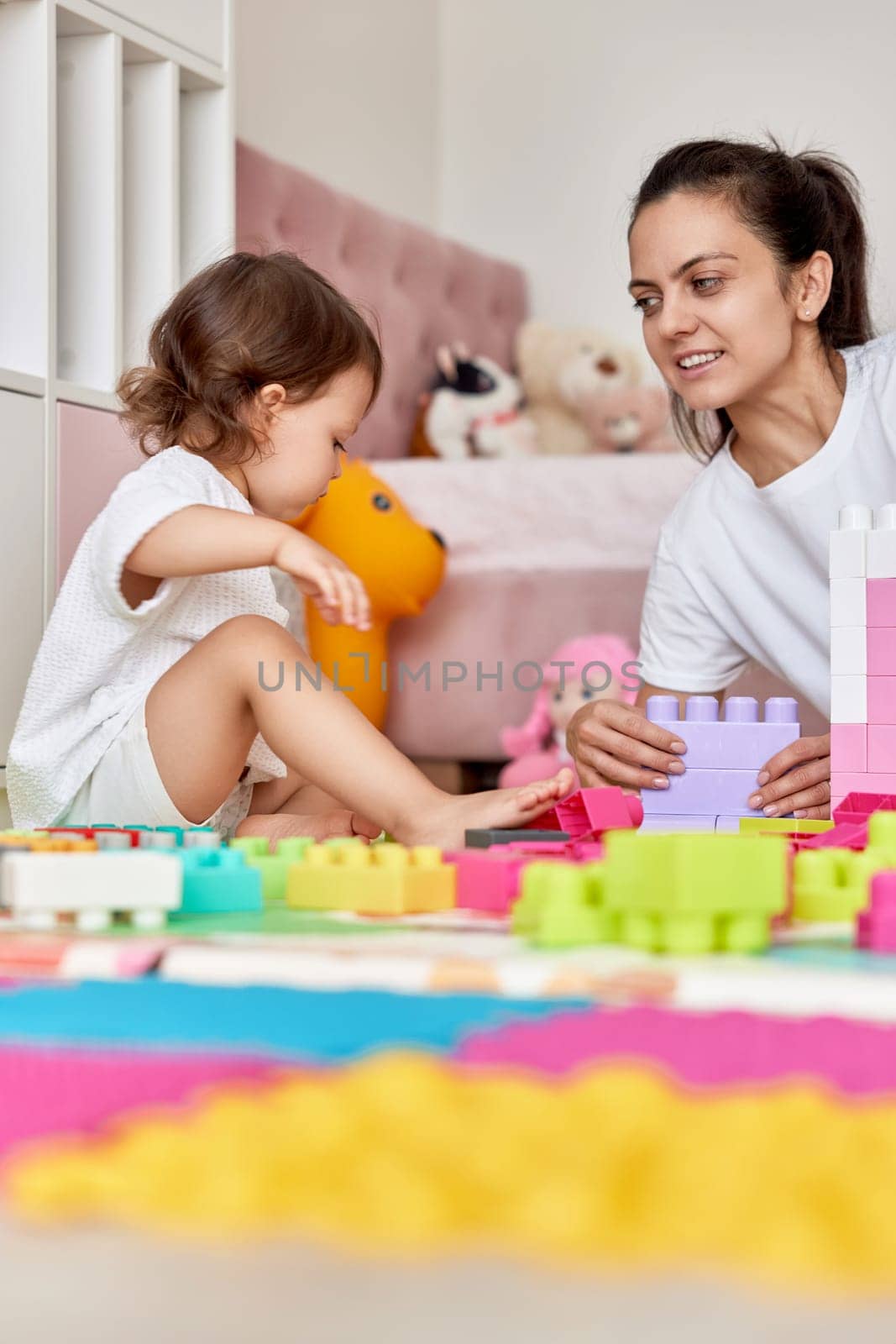 cute baby girl and her loving mother build tower from colorful cubes, having fun together