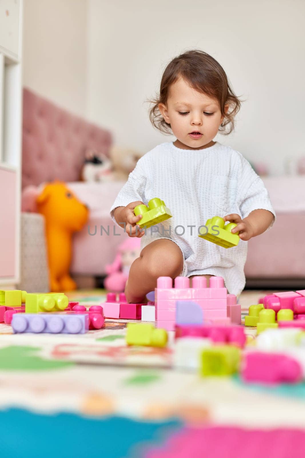 cute baby girl playing with colorful bright cubes in white pink bedroom