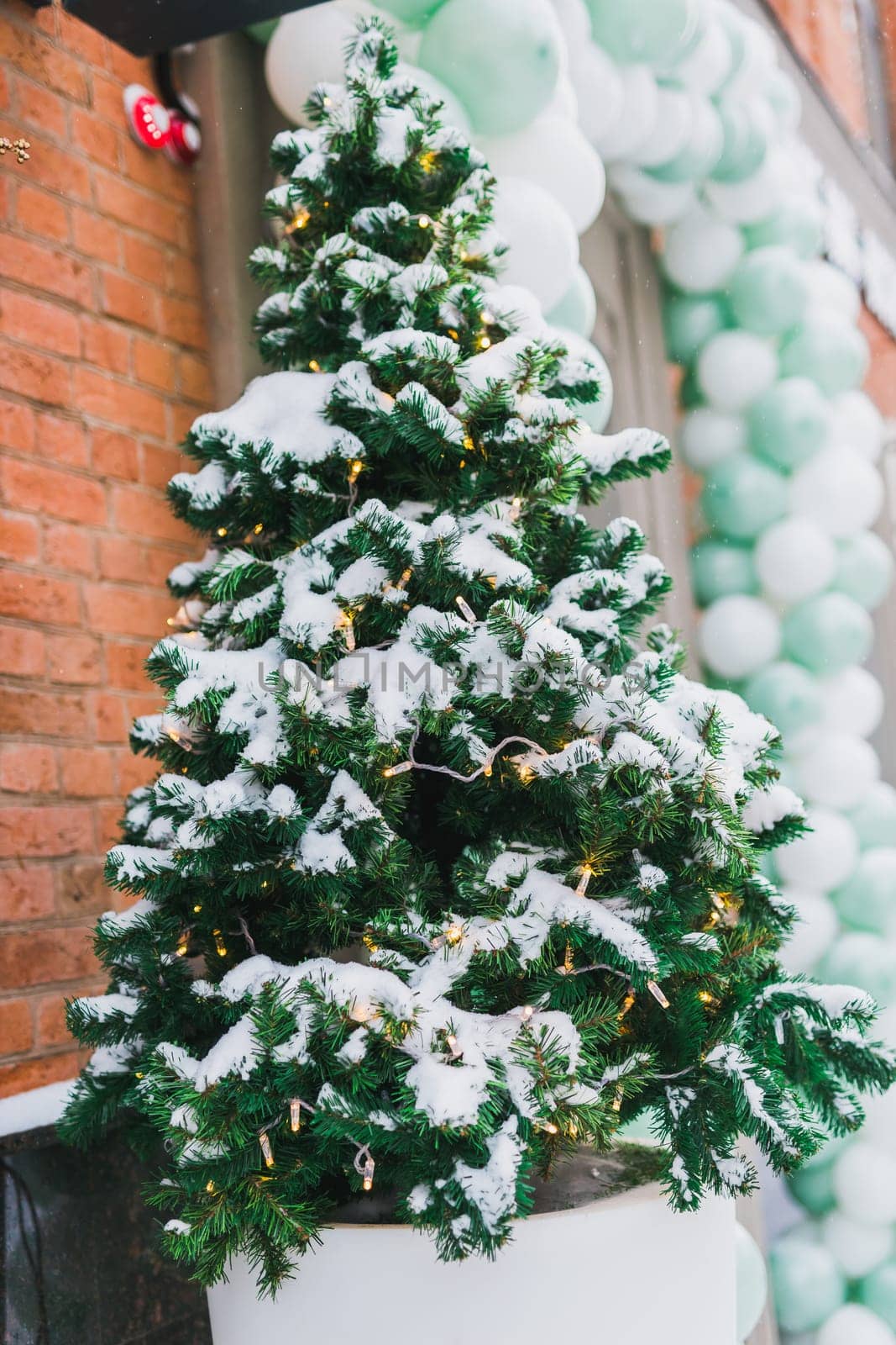 Stylish decorated christmas tree outdoor near store window with snow. Winter holidays and decor for xmas by Satura86