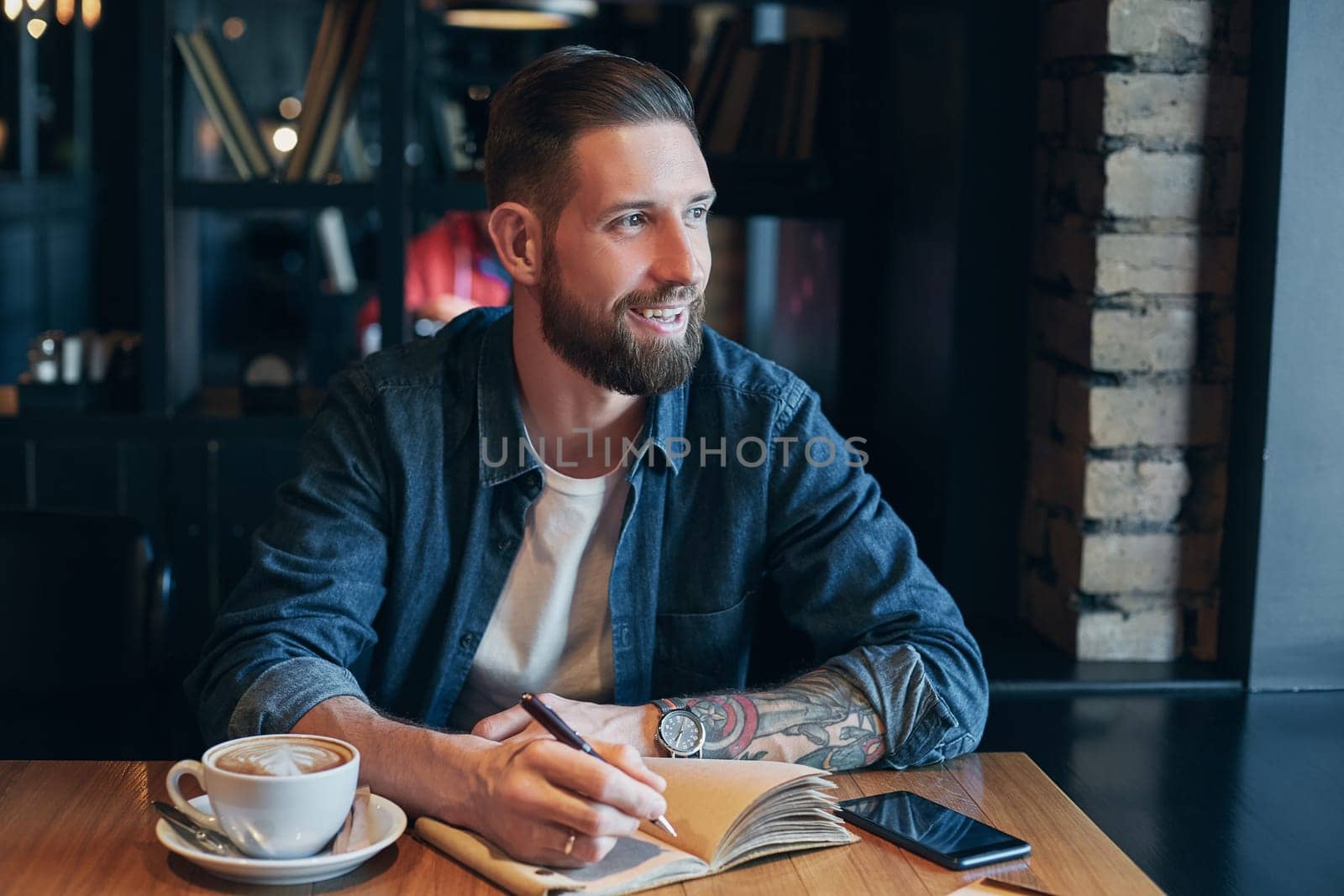 Man hand with pen writing on notebook on a wooden table. Man working at coffee shop