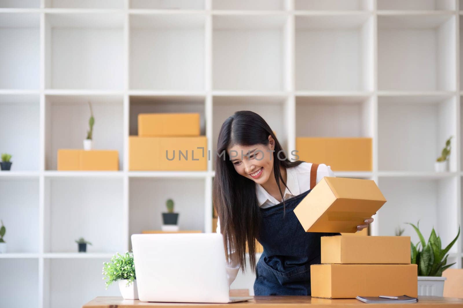 Portrait business woman smile and use laptop checking information on parcel shipping box before send to customer. Entrepreneur small business working at home. SME business online marketing..