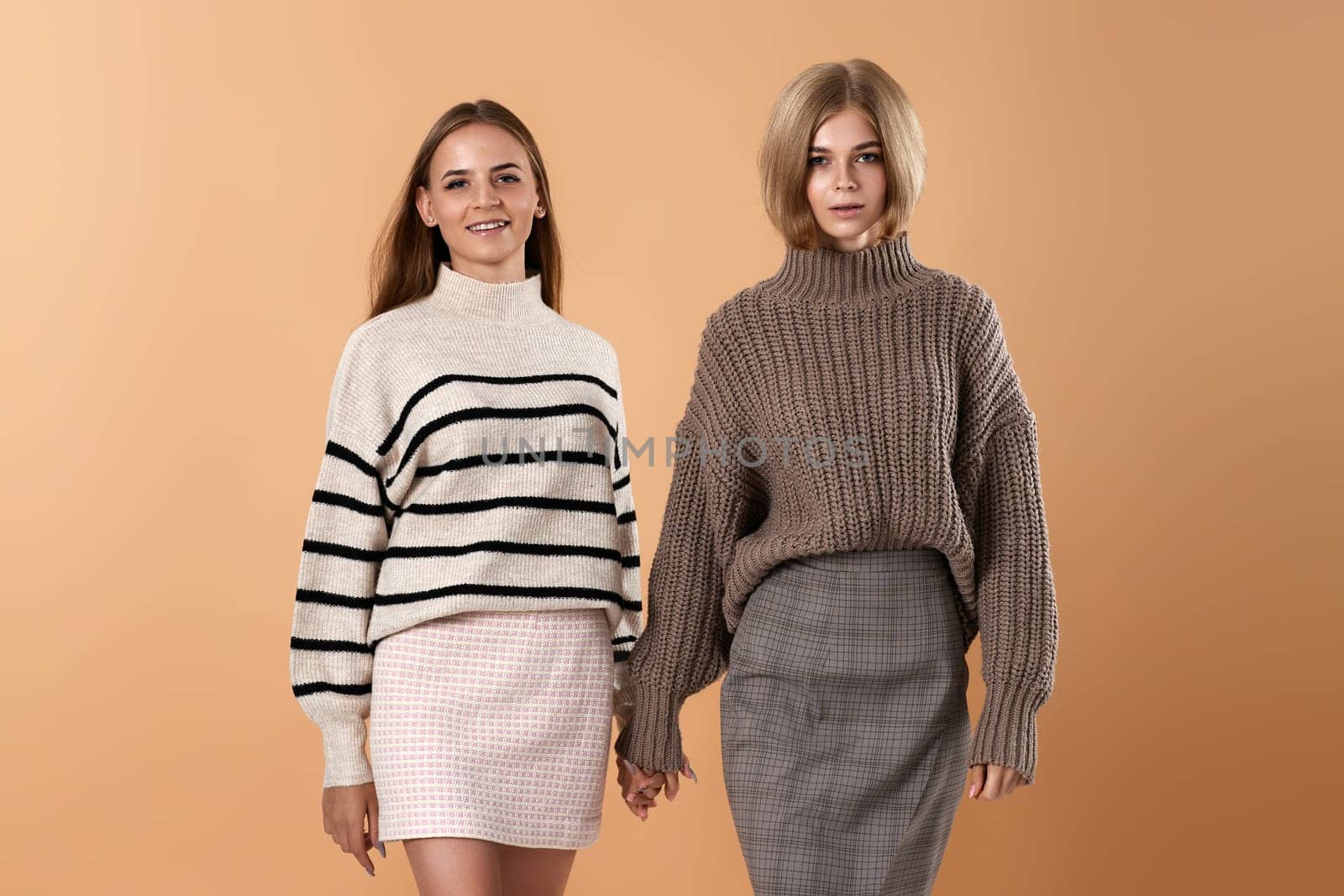 two young women friends hold each other hand walking on beige background