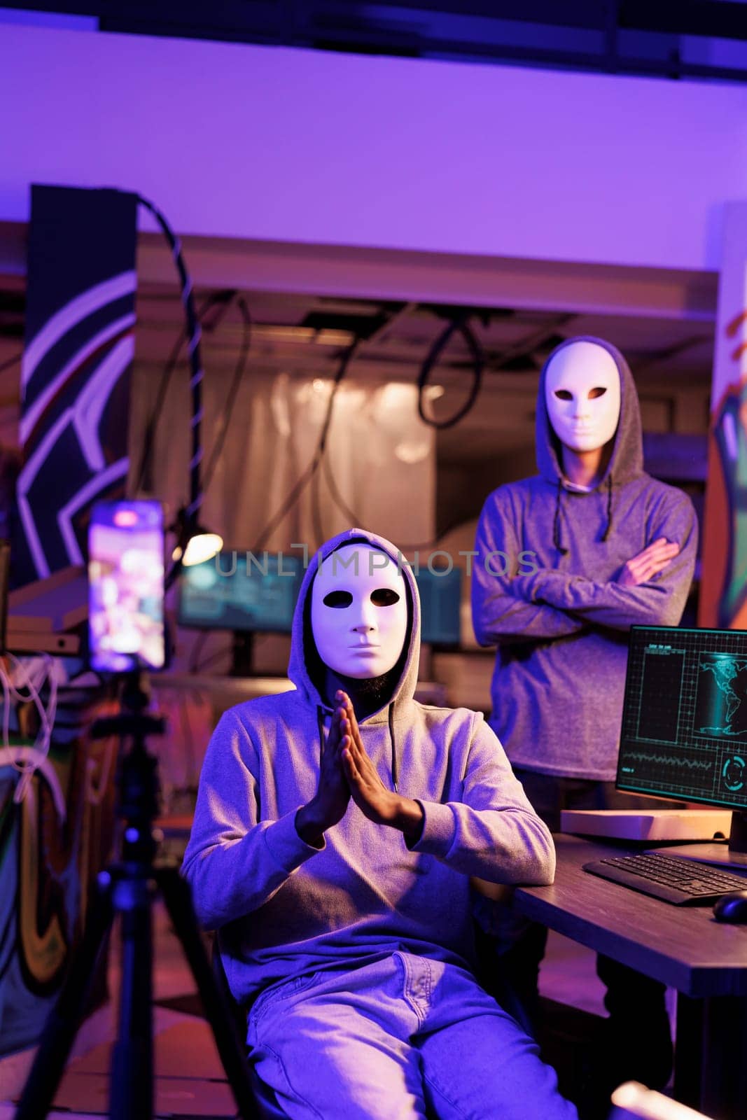 Hackers in masks recording threatening message and demanding victim for confidential privacy information. Anonymous internet scammers doing criminal activities and streaming on mobile phone camera