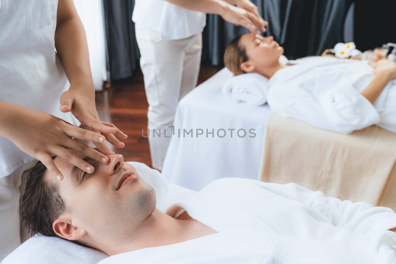 Caucasian couple enjoying relaxing anti-stress head massage and pampering facial beauty skin recreation leisure in dayspa modern light ambient at luxury resort or hotel spa salon. Quiescent