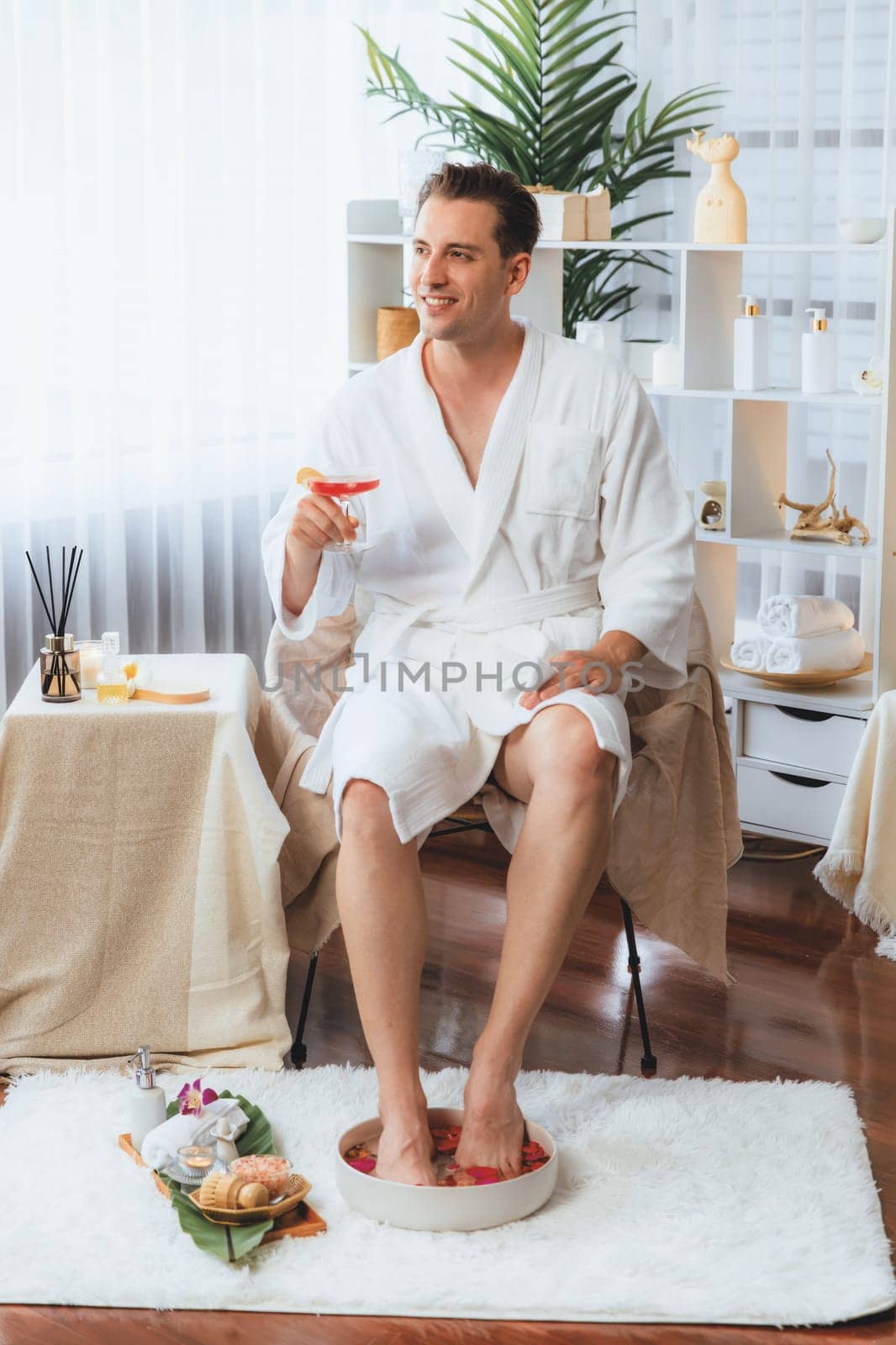 Beauty or body treatment spa salon vacation lifestyle concept with man wearing bathrobe relaxing with drinks in luxurious hotel spa or resort room. Vacation and leisure relaxation. Quiescent