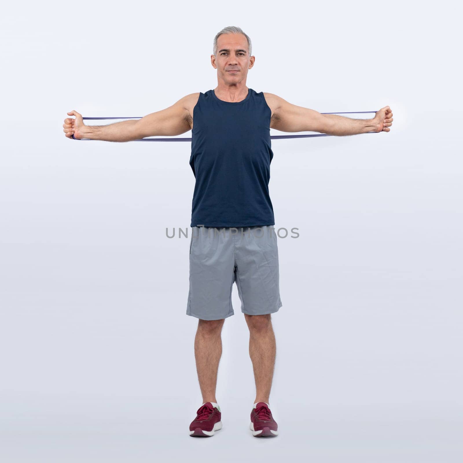 Full body length shot athletic and sporty senior man with fitness resistance band on isolated background. Healthy active physique and body care lifestyle after retirement. Clout