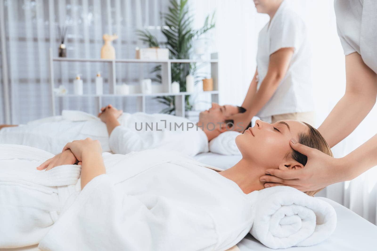 Caucasian couple enjoying relaxing anti-stress head massage and pampering facial beauty skin recreation leisure in dayspa modern light ambient at luxury resort or hotel spa salon. Quiescent