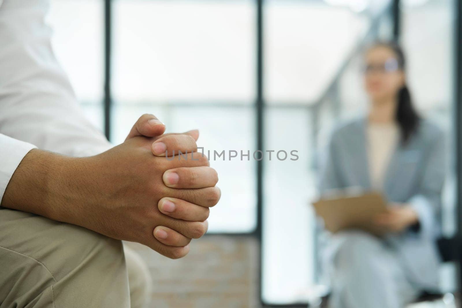 Close up of man hands clenched in stress while discussing his stress, anxiety, and problems with a psychiatrist or therapist at the clinic. by ijeab