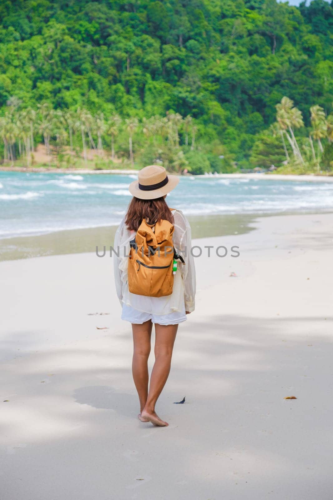 Asian woman with backpack walking at the beach Koh Kood Island Thailand Trat , traveler walking on the beach of the tropical island Ko Kut Island with coconut palm trees on the beach, drone aerial view