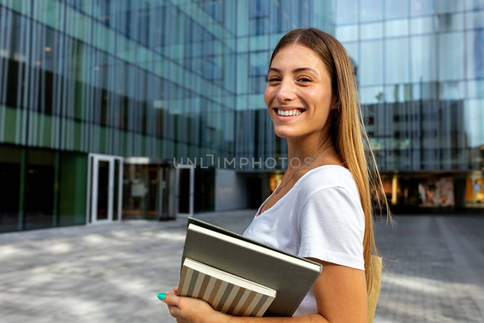 Happy smiling blonde female college student looking at camera holding notebooks. Copy space. by Hoverstock