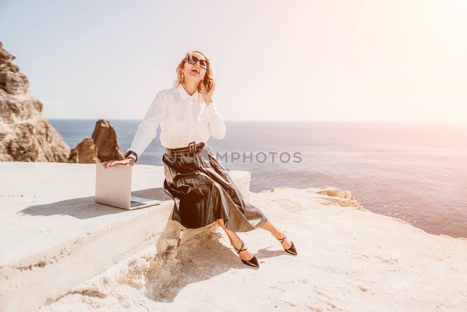 Digital nomad, Business woman working on laptop by the sea. Pretty lady typing on computer by the sea at sunset, makes a business transaction online from a distance. Freelance remote work on vacation