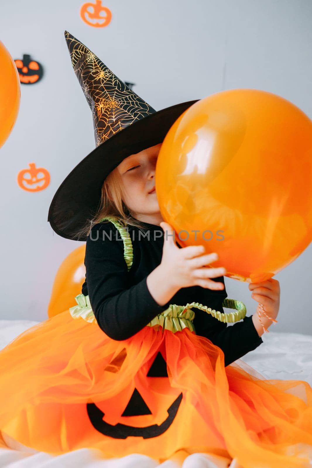 Children's Halloween - a girl in a witch hat and a carnival costume with airy orange and black balloons at home. Ready to celebrate Halloween.