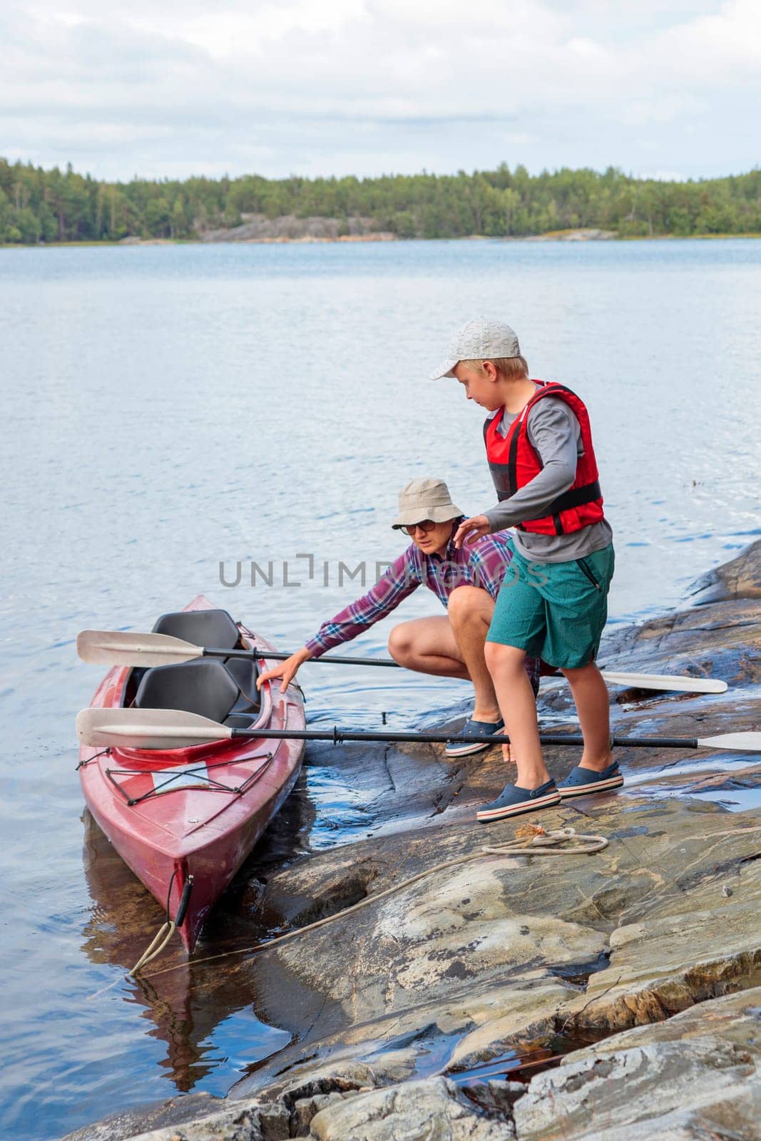 Father and son are preparing kayak and paddles for kayaking by the sea, canoeing, boating in the Baltic sea during family summer vacations in Finland, vertical