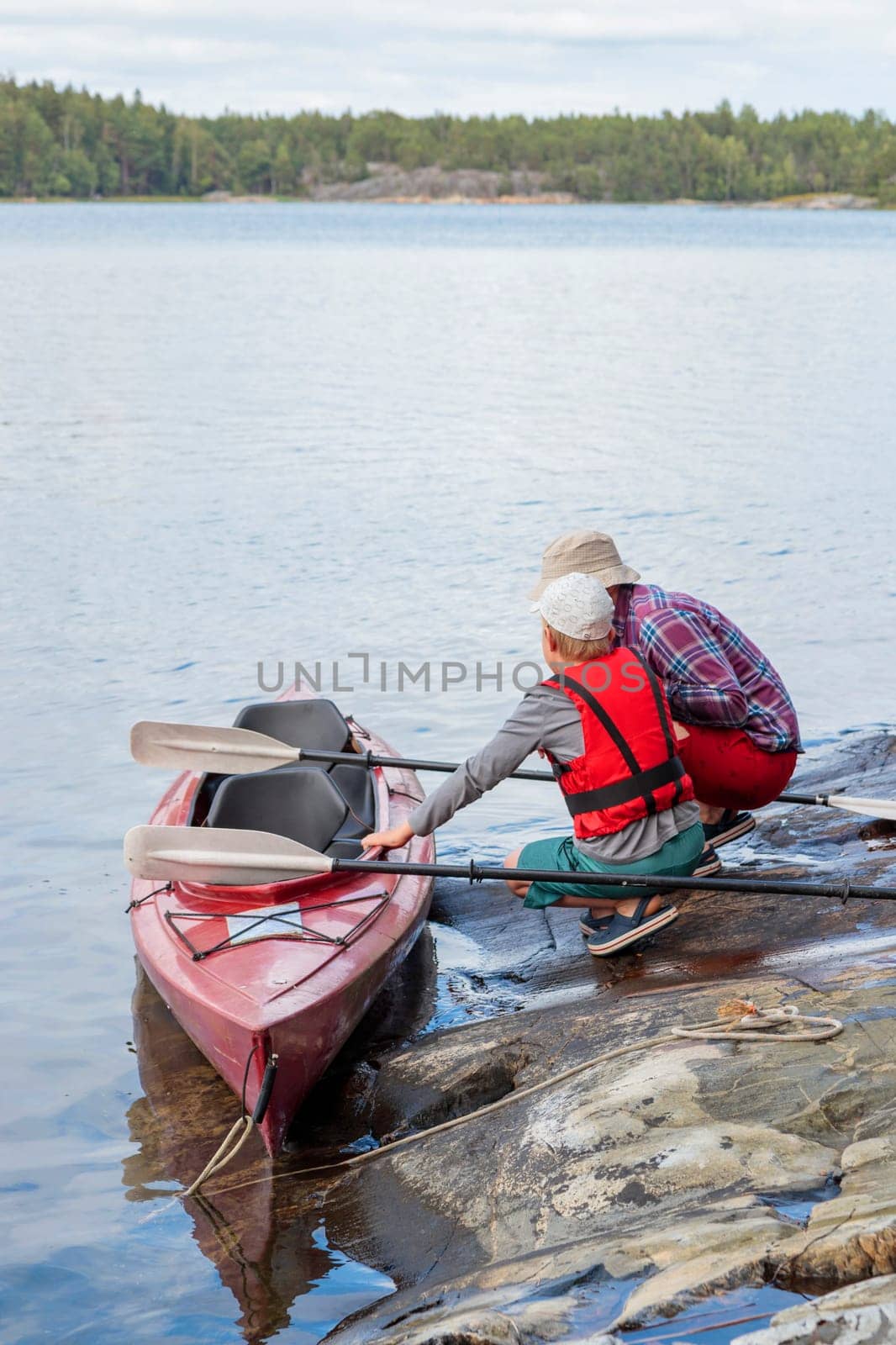 Father teaches his son for kayaking by the sea with paddles for kayaking by the sea, canoeing, boating in the Baltic sea during family summer vacations in Finland, vertical