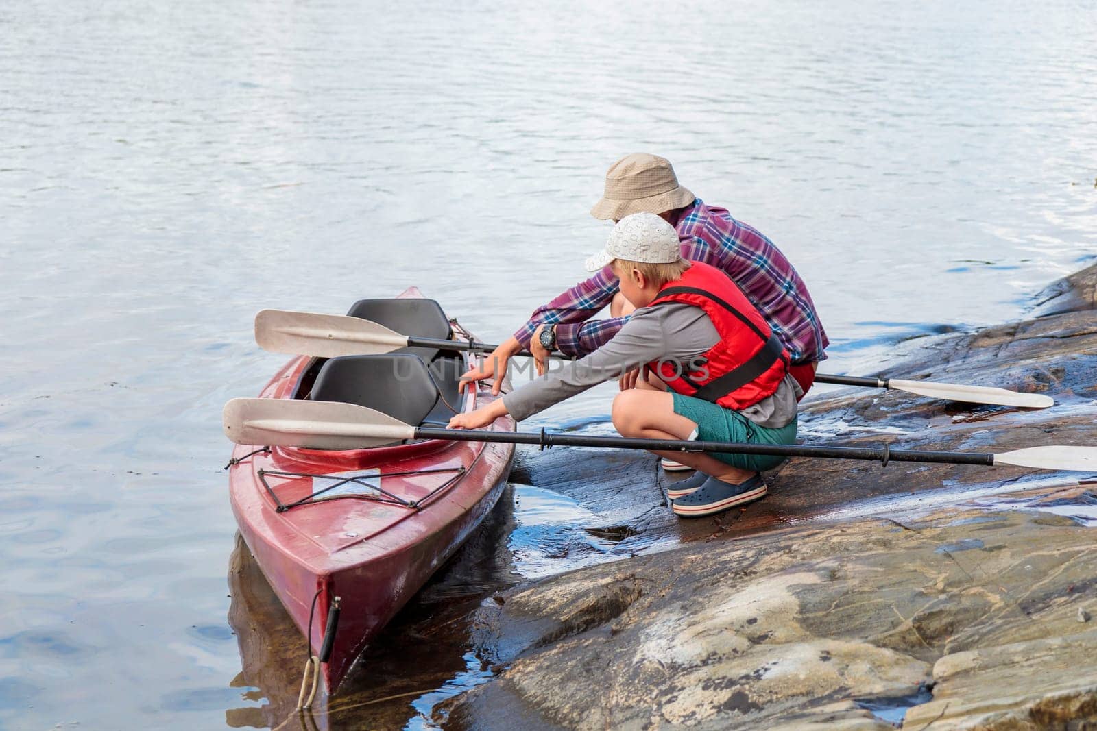 Father teaches his son for kayaking by the sea with paddles for kayaking by the sea, canoeing, boating in the Baltic sea during family summer vacations in Finland, horizontal