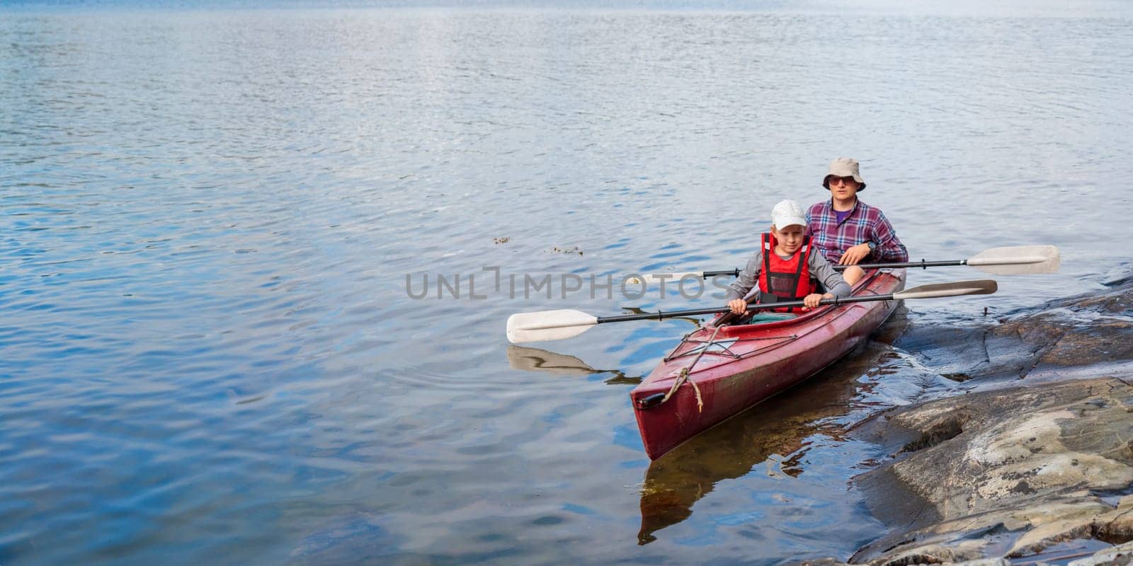 Father and son are starting to go by kayak with paddles, kayaking, canoeing, boating in the Baltic sea during family summer vacations in Finland, banner horizontal