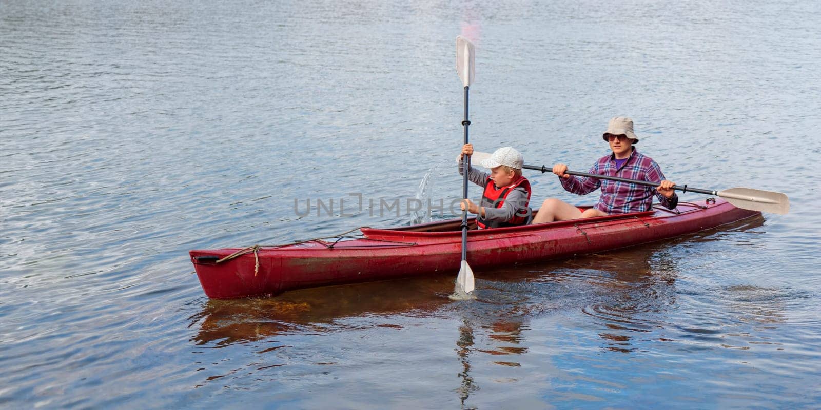 Father teaches his son for kayaking by the sea with paddles for kayaking by the sea, canoeing, boating in the Baltic sea during family summer vacations in Finland, horizontal banner