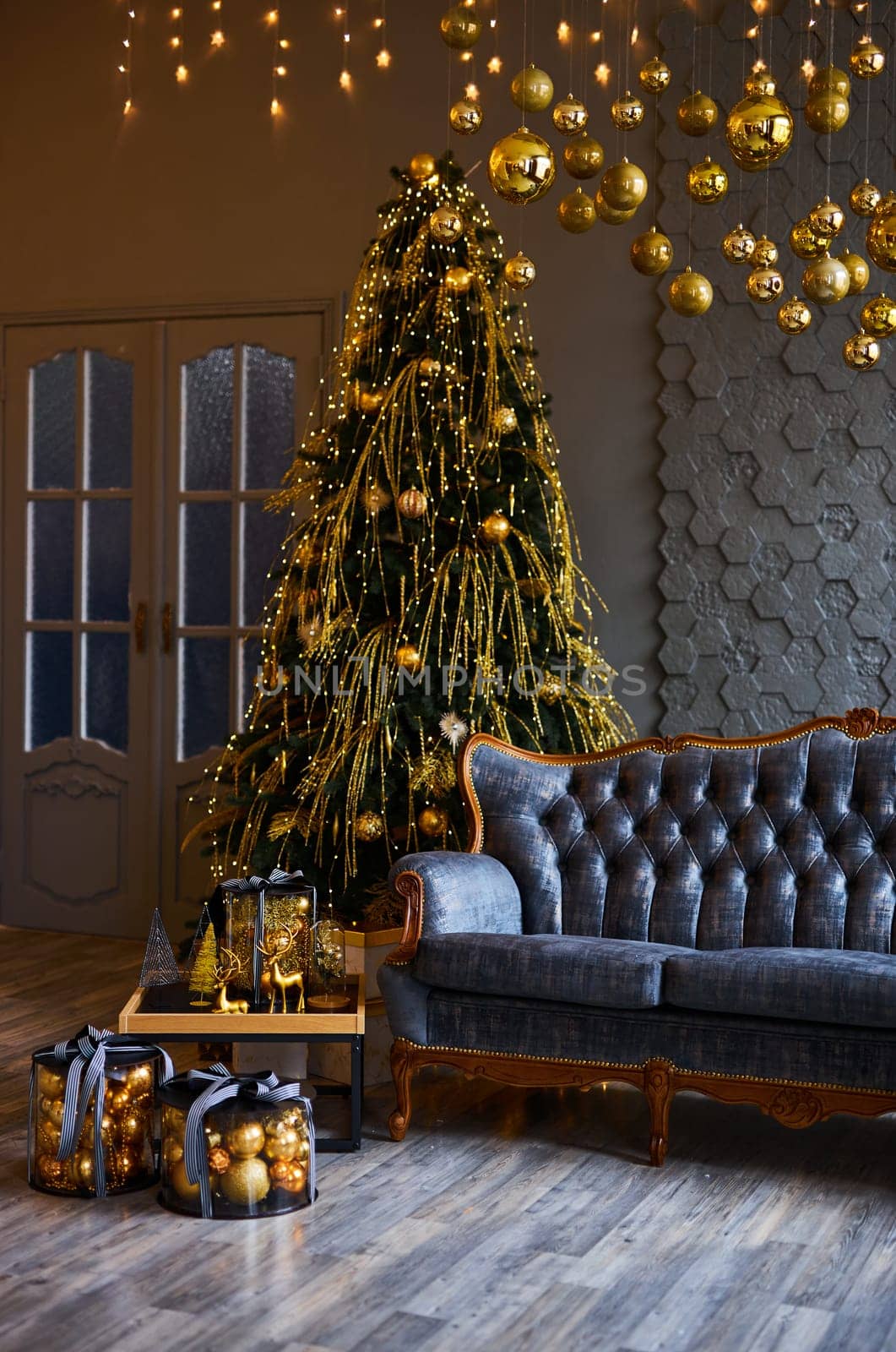 Luxurious interior of the room for Christmas and New Year. Living room in gray and gold tones with a sofa, many gifts, golden balls, ice lights, two Christmas trees