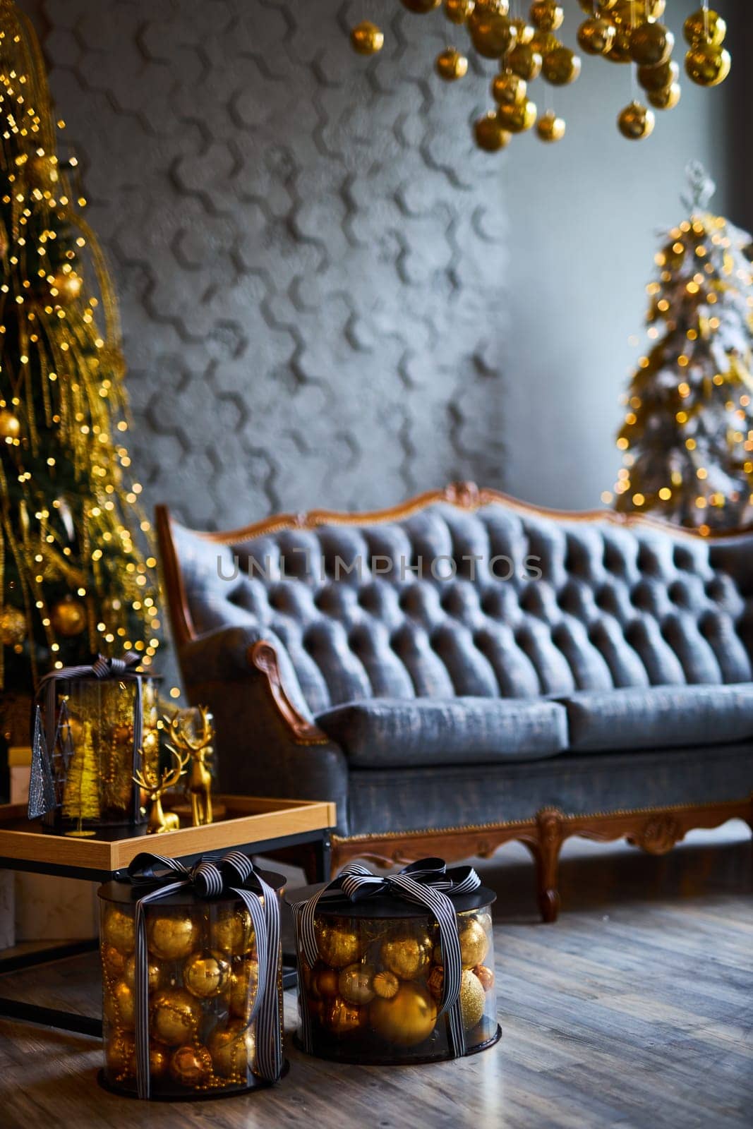 Luxurious interior of the room for Christmas and New Year. Living room in gray and gold tones with a sofa, many gifts, golden balls, ice lights, two Christmas trees
