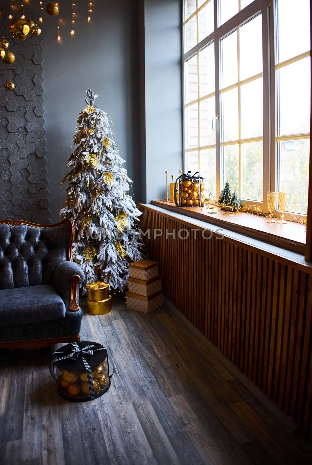 Luxurious interior of the room for Christmas and New Year. Living room in gray and gold tones with a sofa, many gifts, golden balls, ice lights, two Christmas trees