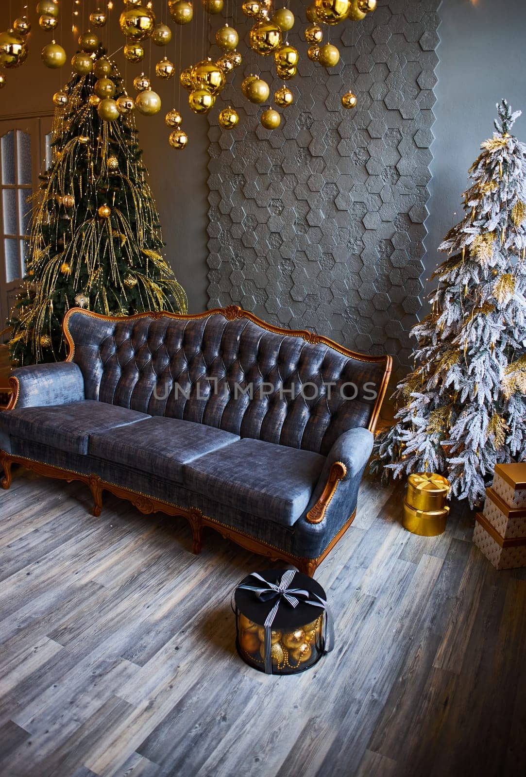 Luxurious interior of the room for Christmas and New Year. Living room in gray and gold tones with a sofa, many gifts, golden balls, ice lights, two Christmas trees