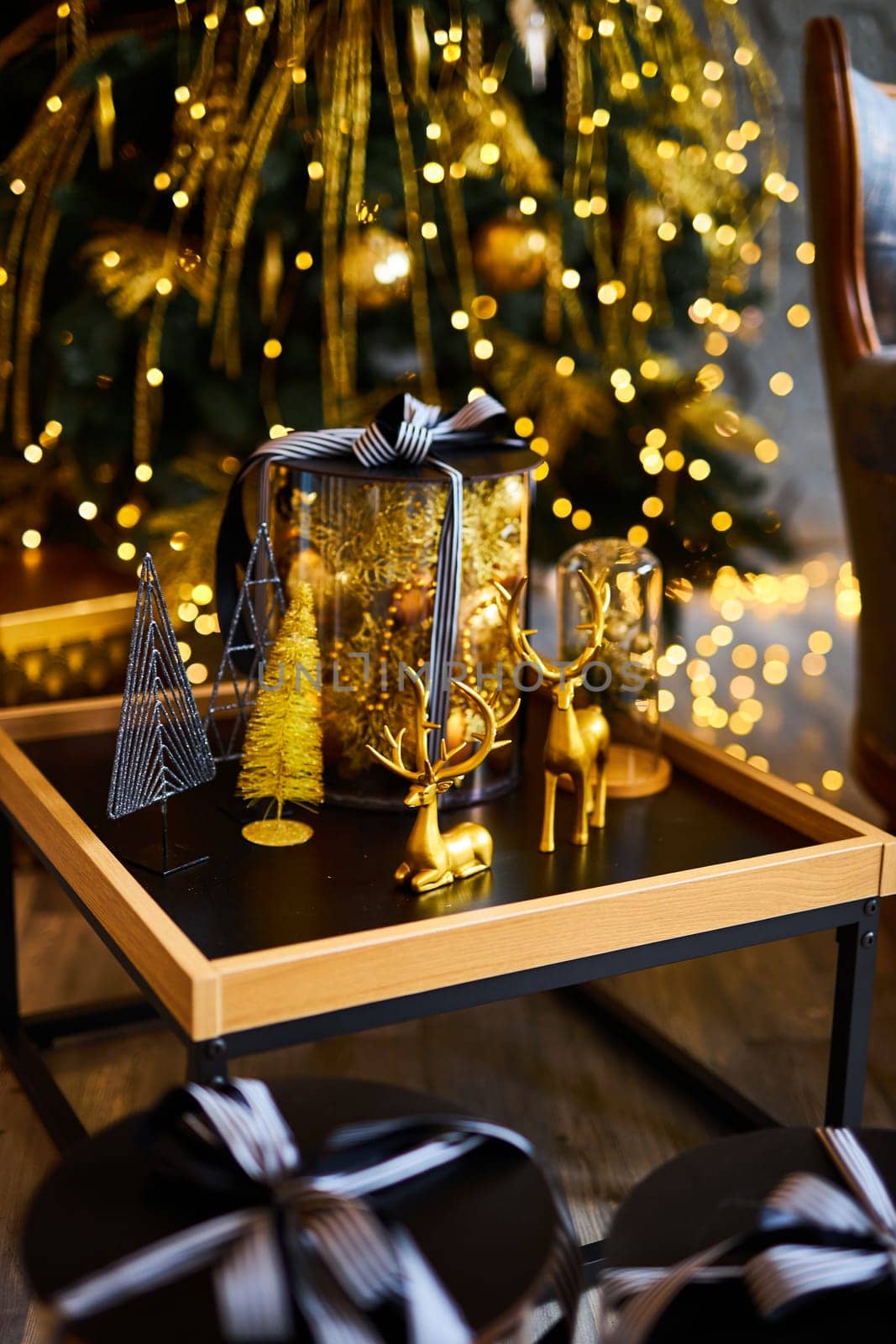 Luxurious interior of the room for Christmas and New Year. Living room in gray and gold tones with a sofa, many gifts, golden balls, ice lights, two Christmas trees
