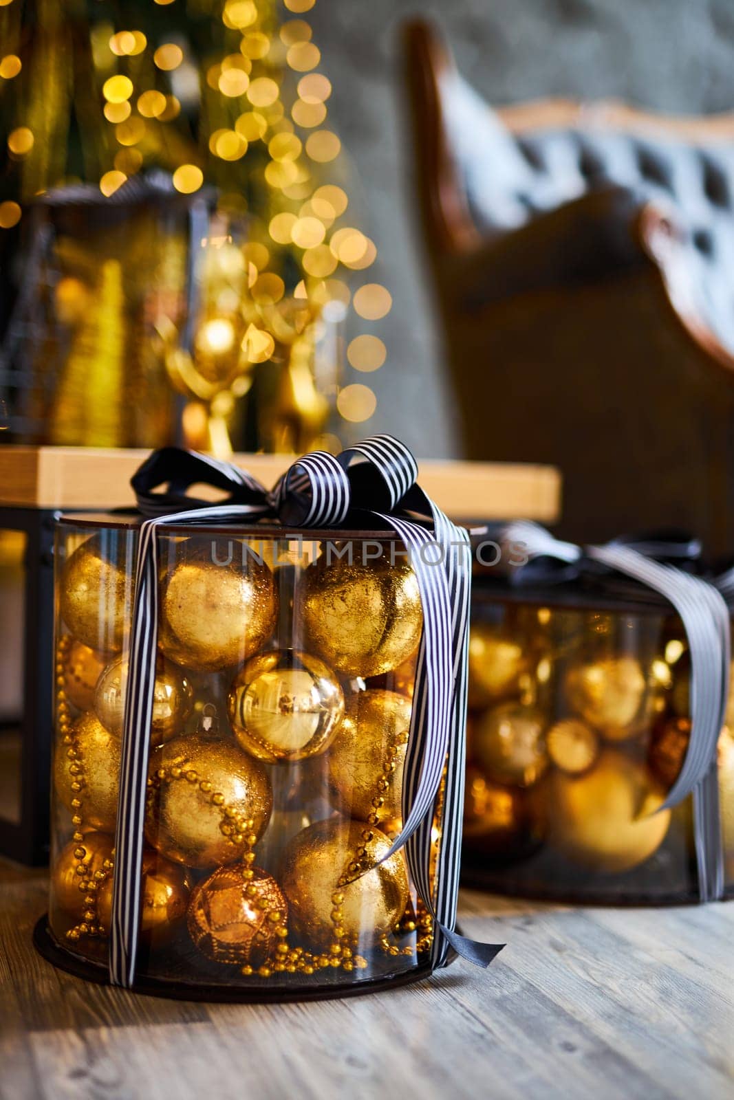 Luxurious interior of the room for Christmas and New Year. Living room in gray and gold tones with a sofa, many gifts, golden balls, ice lights, two Christmas trees