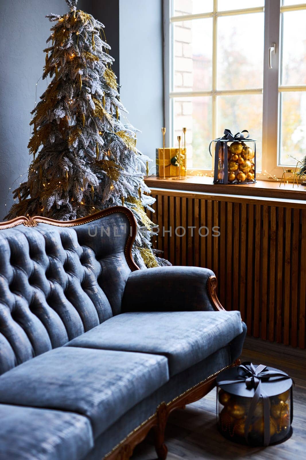 Luxurious interior of the room for Christmas and New Year. Living room in gray and gold tones with a sofa, many gifts, golden balls, ice lights, two Christmas trees
