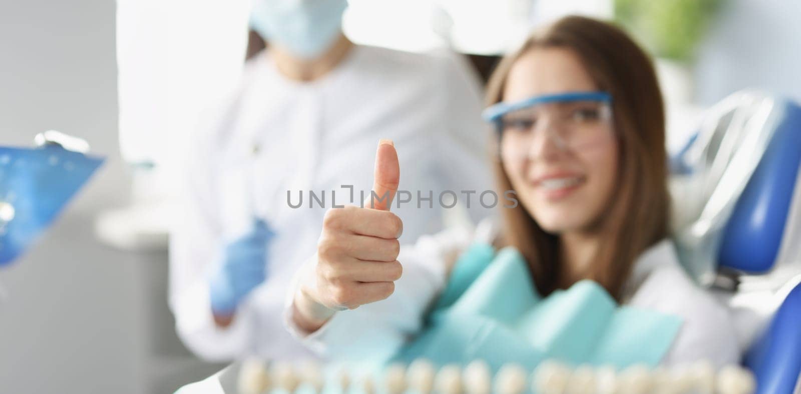 A woman at the dentist shows a thumbs up gesture, blurry, close-up. Professional dental care, satisfied patient