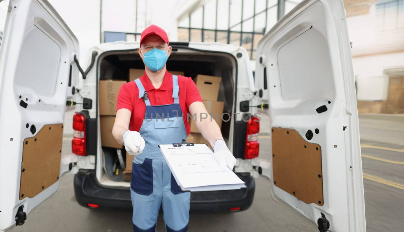A male courier holds out documents for signature. Delivery of parcels around the city during a pandemic