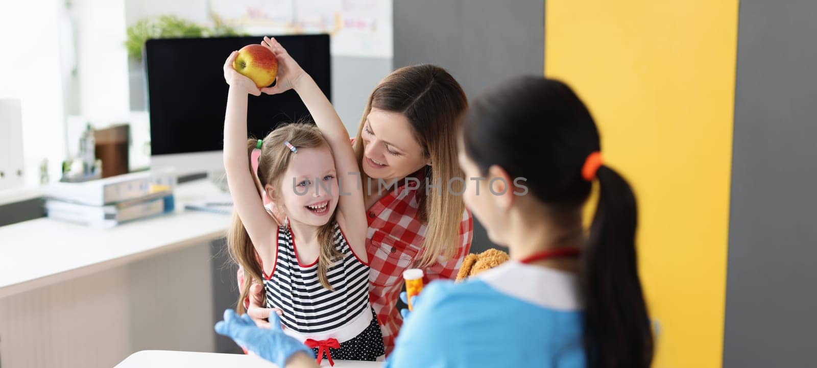 A little girl with her mother at the doctor rejoices at an apple, close-up. Consultation with a pediatric nutritionist, natural and synthetic vitamins