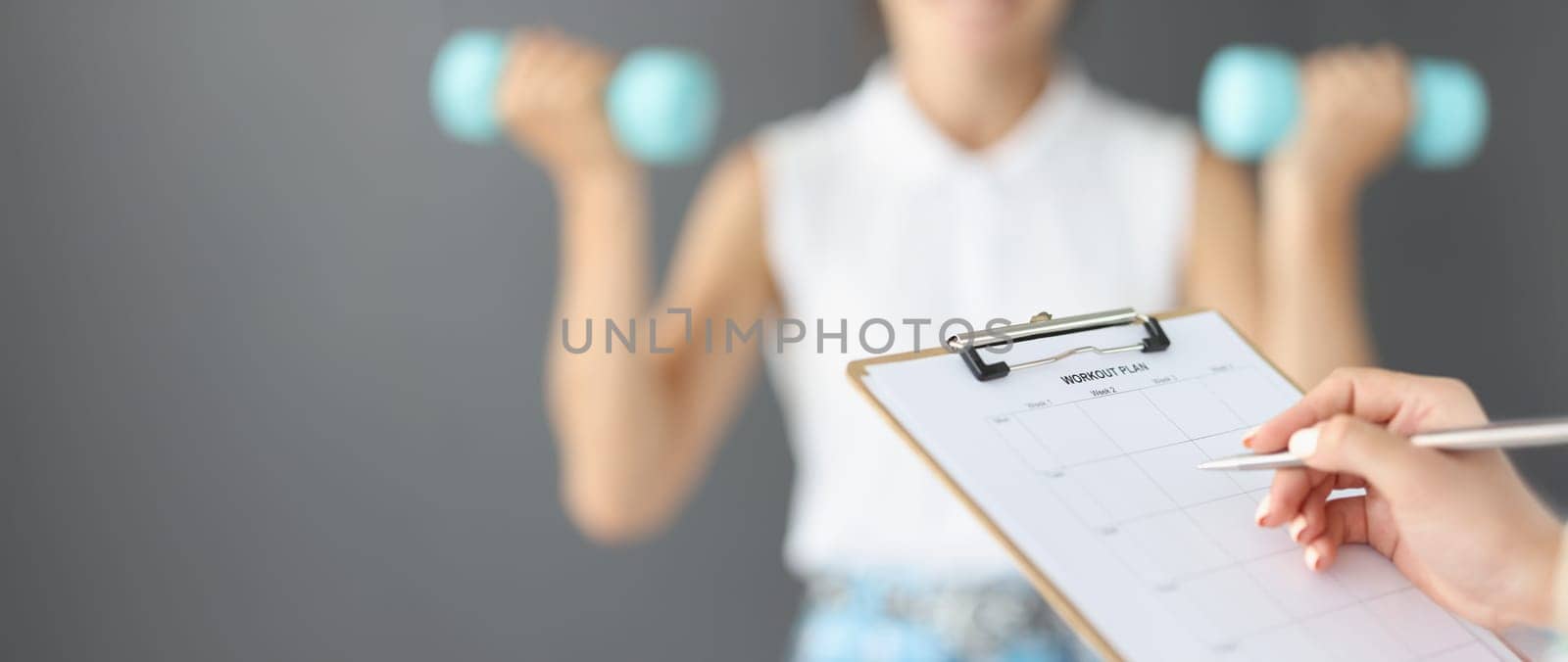 Female hands are writing down a workout plan, close-up, blurry. Fitness trainer control, exercises with dumbbells